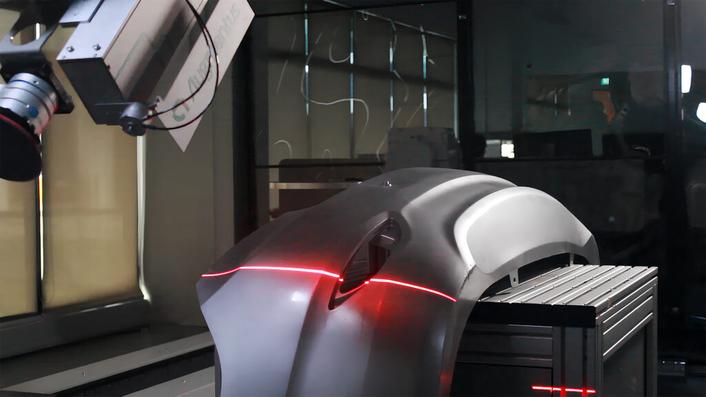 A laser scanner attached to a robot arm captures scan data of a car bumper for sanding