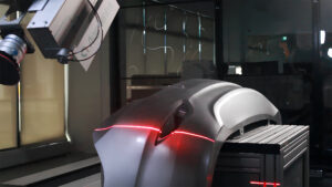 A laser scanner attached to a robot arm captures scan data of a car bumper for sanding