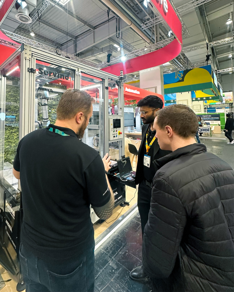Members of Augmentus' and Servind's teams engaging with a booth visitor, who is viewing a live robot demonstration of our scan-to-path process.